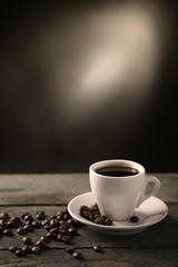 Cup of coffee and coffee grains on wooden table, on gray background