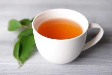 Ceramic cup of tea with green leaves on light wooden background