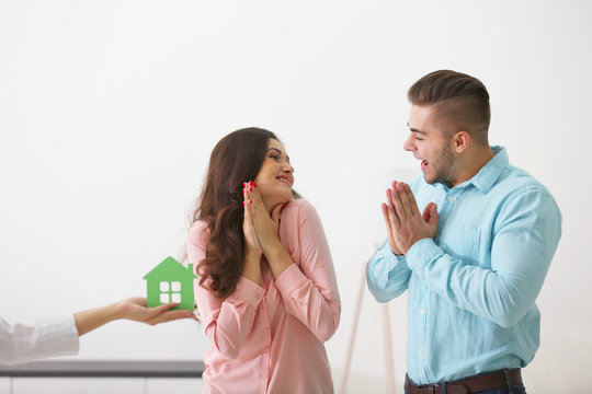 Hands of estate agent giving model of house to  couple, on light background