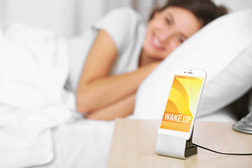 Beautiful young woman waking up with mobile alarm clock