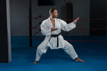 Fototapety  Mężczyzna w białym kimonie i czarnym pasie trenujący karate