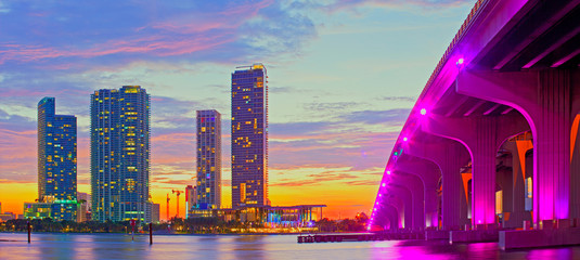 Fototapeta premium Miami na Florydzie o zachodzie słońca, kolorowa panorama oświetlonych budynków i most na grobli Macarthur