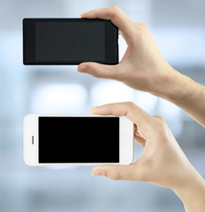 Hands holding black and white smart phones on light background