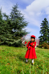 Cute little girl dressed in red coat and hat on green grass fiel