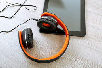 Headphones with tablet on wooden table close up