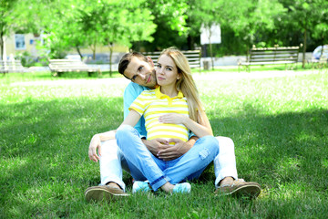 Fototapeta premium Young pregnant woman with husband sitting on green grass in park