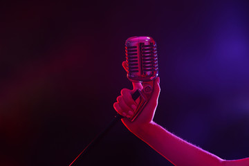 Female hand holding a retro microphone against colourful background