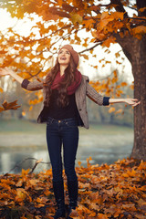slender young brunette beautiful girl with long hair in a beret with a scarf and coat walks in autumn park with a lot of yellow and orange leaves
