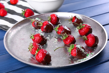A plate of strawberries in chocolate on blue wooden background