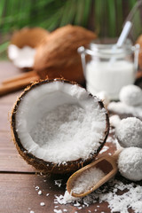 Candies in coconut flakes, glass of milk and fresh coconut on dark wooden background