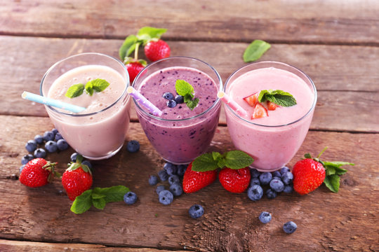 Tasty blueberry, strawberry and milk yogurts in a row decorated with berries and mint on wooden background