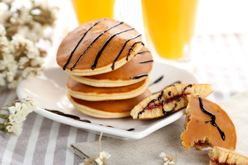 Tasty pancakes with jam on white plate with orange juice and flowers, close up