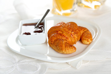 Plate of croissant, jam and orange juice on white table