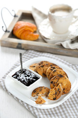 Plate of tasty cookies with chocolate crumbs and jam against cup of coffee on wooden tray