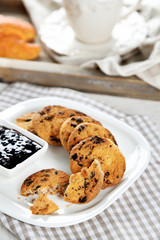 Plate of tasty cookies with chocolate crumbs and jam against cup of coffee on wooden tray