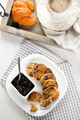 Plate of tasty cookies with chocolate crumbs and jam against cup of coffee on wooden tray