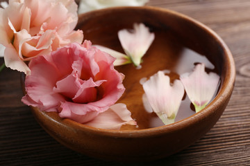Pink rose and petals in a bowl of water on wooden background