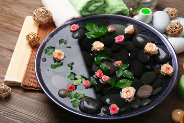 Spa composition of candles, flowers and stones in water, on wooden background