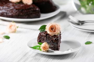 Piece of chocolate cake decorated with flowers on white wooden table