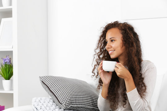 Pretty young woman drinking coffee on sofa at home