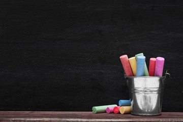 Multicoloured chalk in a metal bucket on blackboard background