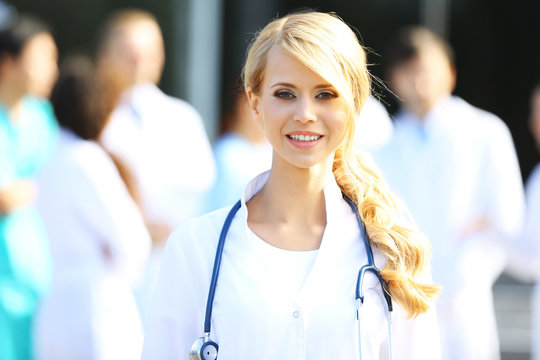 Beautiful smart woman doctor standing against blurred group of medics