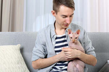 Young handsome man holding a cat on light room background