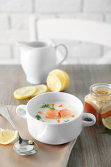 Delicious salmon cream soup on wooden table, which served with sliced lemon and spices