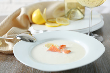 Served wooden table with tasty salmon cream soup, wine and lemon on it, close up
