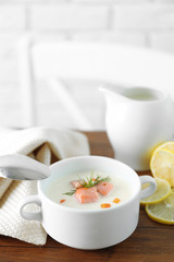 Delicious salmon cream soup with spoon on wooden table, which served with sliced lemon and spices