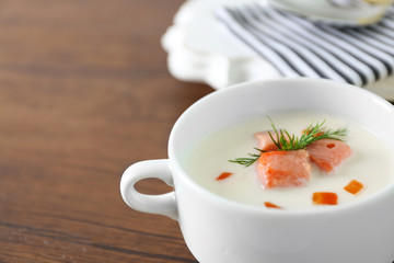 Delicious salmon cream soup in white bowl with lemon and striped cotton serviette on wooden table, close up