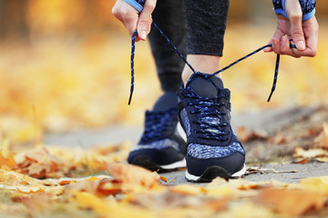 Woman in sportswear tying shoelaces on sneakers outdoor close-up - obrazy, fototapety, plakaty