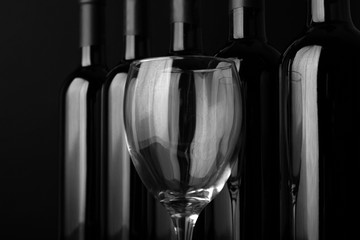 Glass and wine bottles in a row on black  background, close up