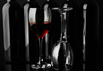 Wine glasses against bottles in a row on black background, close up