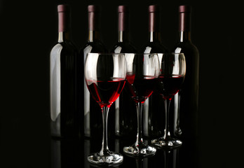 Wine glasses against bottles in a row on black background, close up