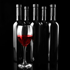 Red wine glass against bottles in a row on black background, close up