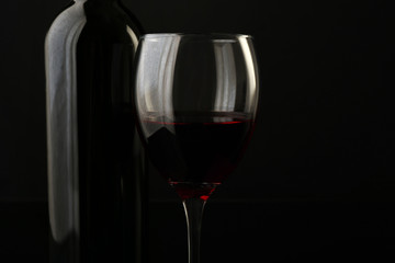 Red wine glass and bottle on black background, close up