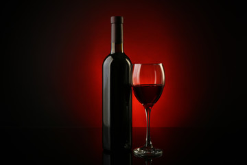 Wine glass and bottle on dark red background, close up
