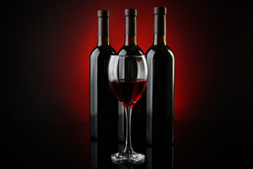 Wine glass against bottles in a row on dark red background, close up