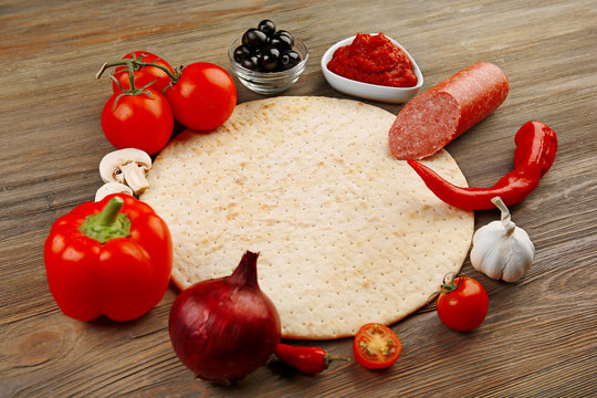 Dough basis and ingredients for pizza in the shape of circle, on the table