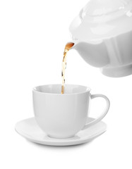 Tea flows from a teapot in a cup isolated on white background