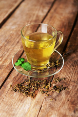 Glass cup of tea with mint leaves and herbs on wooden background