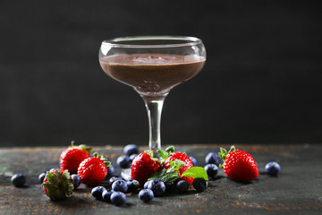 Chocolate dessert in glass and fresh berries on color wooden background