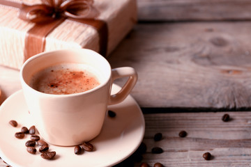 Beautiful gift, cup with coffee and coffee grains on wooden background