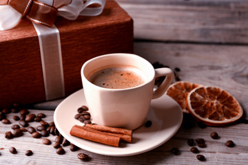 Beautiful gift, cup with coffee and coffee grains on wooden background