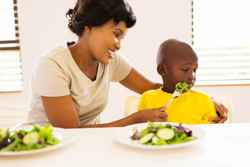african mother trying to feed her little son green salad