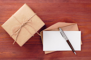 Gift box and envelope with blank paper sheet and pen on wooden table
