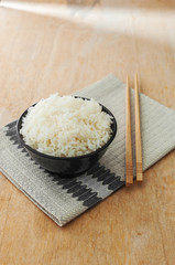 White rice in black bowl with wood chopsticks