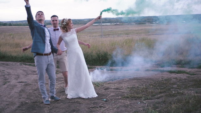 The bride, the groom and his friend posing in a field with smoke bombs