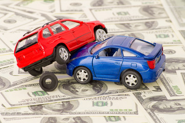Toy cars in accident on a background of 100 dollar bills
